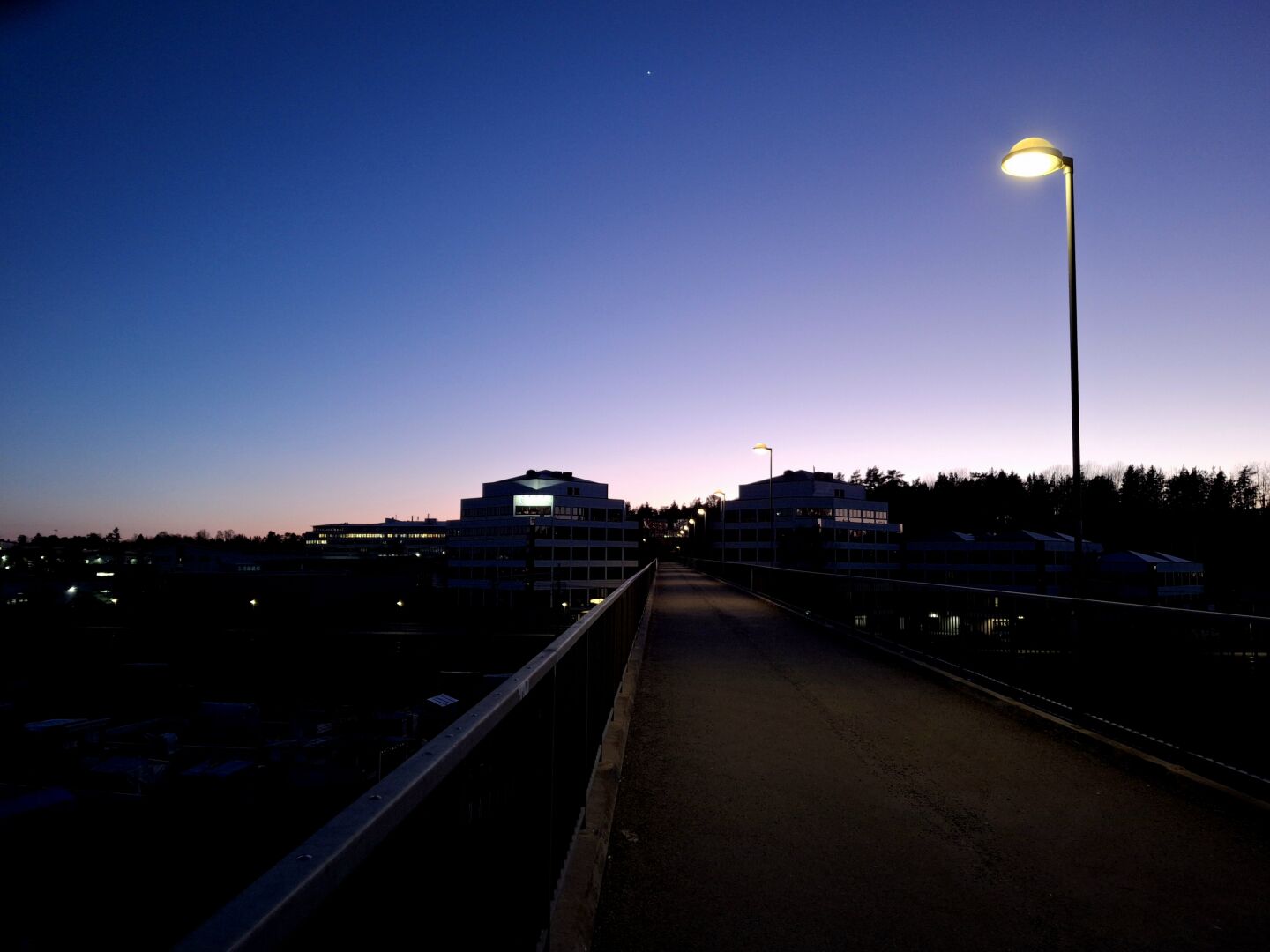 View of very dark industrial suburb with a clear sky winter sunset. The sky is fading from white-pink to dark blue. Venus as a small bright star in the sky.