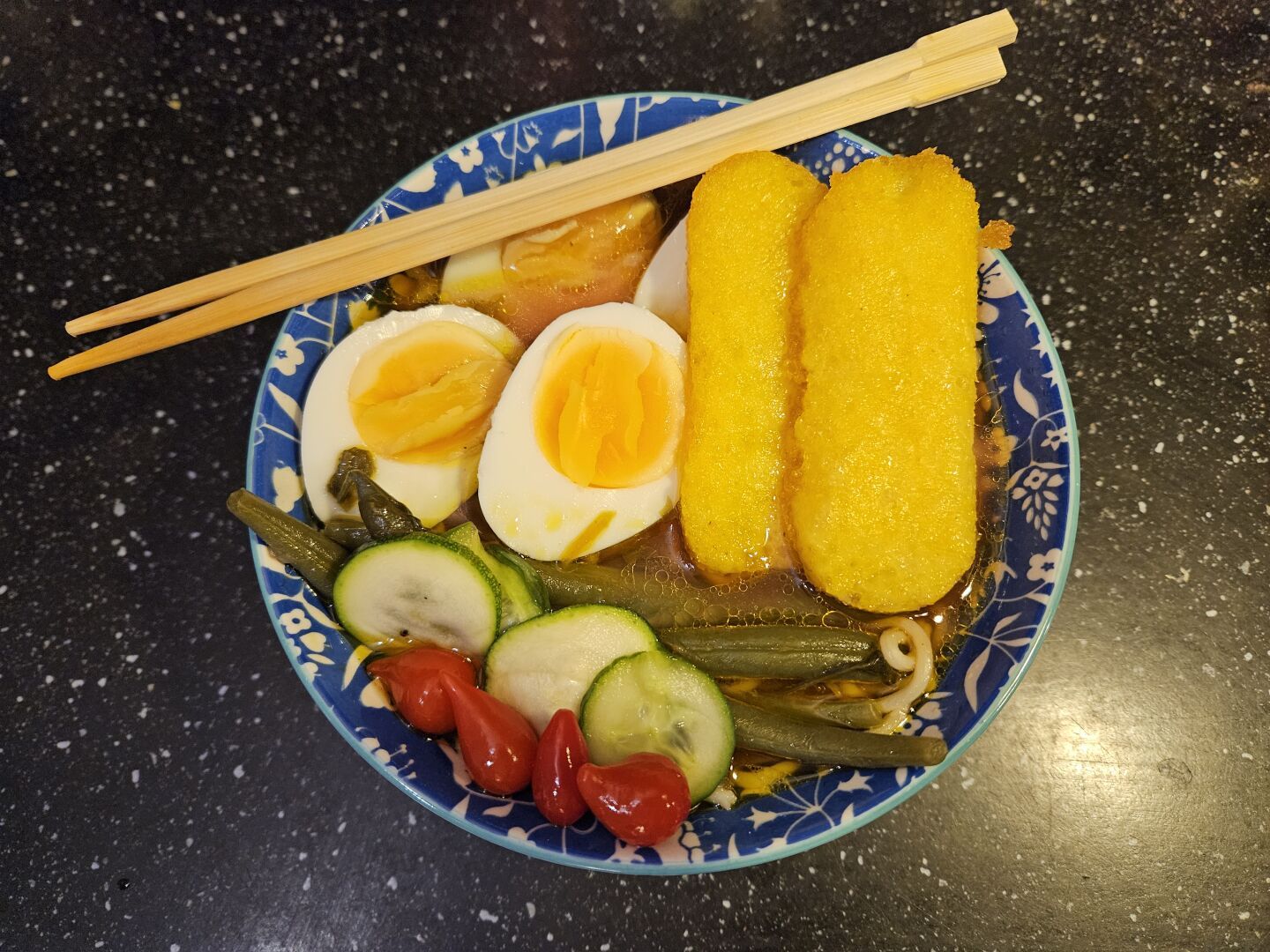 Blue bowl with four egg helves, two pieces of polenta, string beans, and red and green pickles.