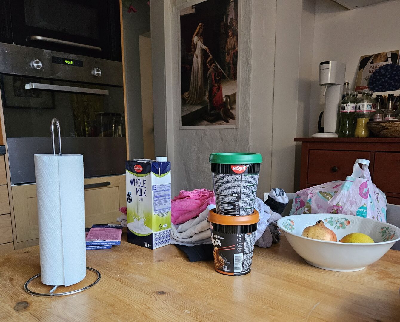 My kitchen table, filled with clean laundry, Nissin Soba noodle cups, long-life milk, and chocolate.