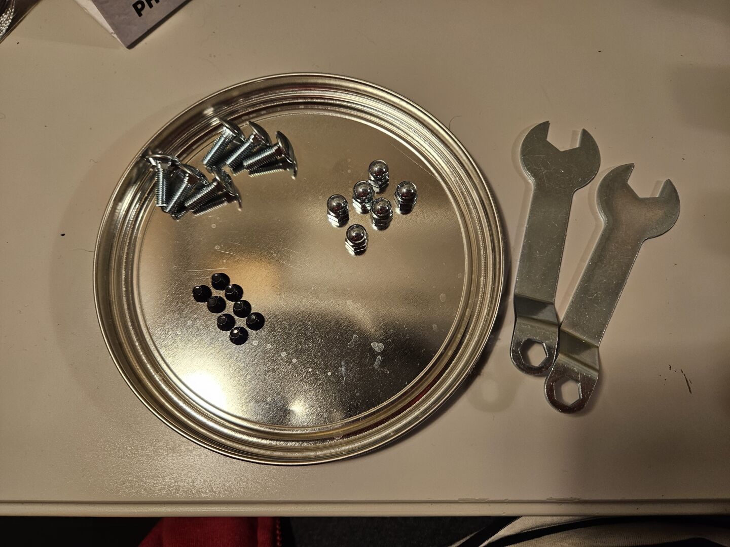 A small tin lid, turned upside down to form a tray. Inside are the screws and bolts needed to assemble the cary.