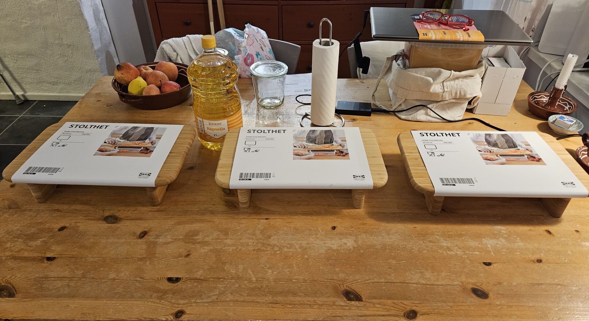 Three bamboo cutting boards on "legs" standing on a kitchen table. The IKEA wrappings are left on, revealing them to be the item STOLTHET.