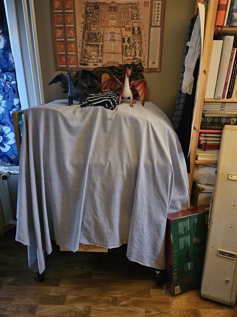 My sewing station and wild card in the upcoming rearrangement of furniture. It looks like three ghosts hidden under a checkered sheet, wearing two dragons and a cross as hats.
