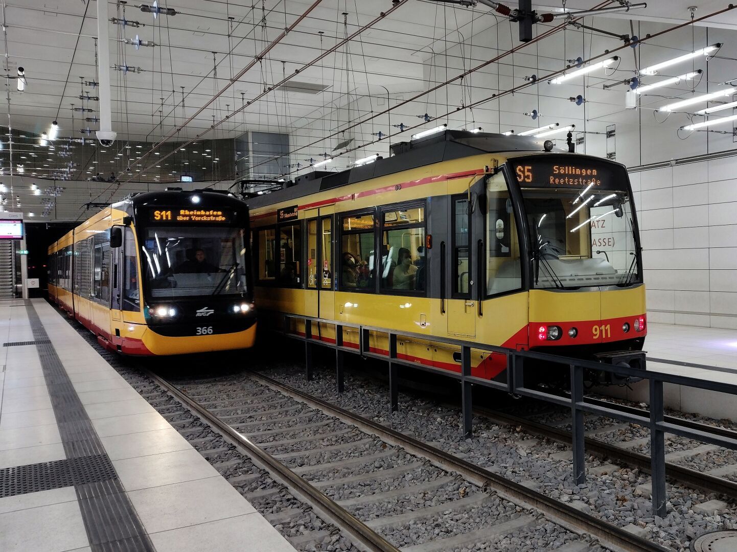 Ein Einsystem-Stadtbahnwagen des Typs NET2012 fährt als Einrücker der Linie S11 zum Rheinhafen (Betriebshof West) in die Haltestelle Karlsruhe Marktplatz (Kaiserstraße) ein. Auf dem Gleis dahinter steht ein Zweisystem-Stadtbahnwagen auf der Linie S5 nach Söllingen Reetzstraße.