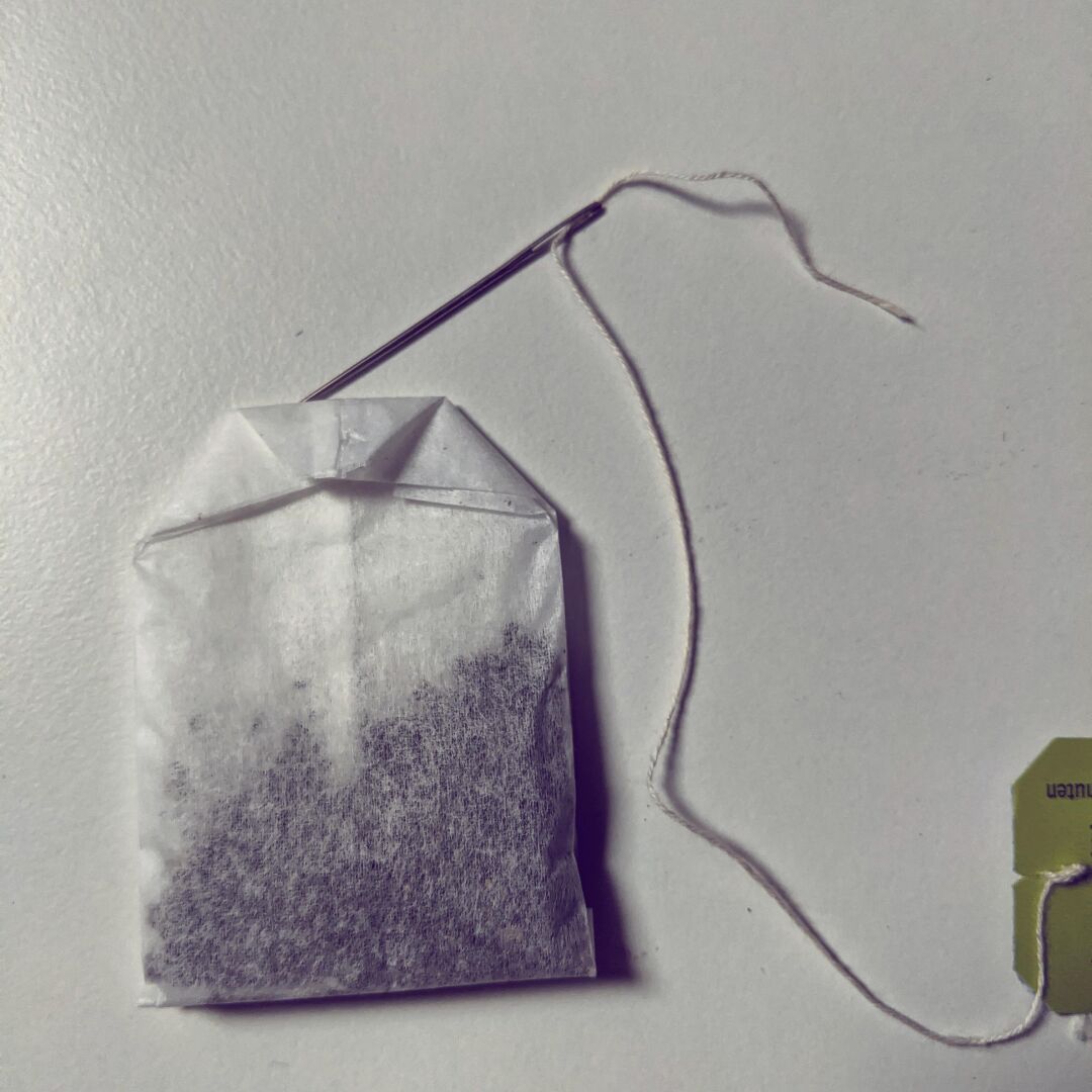 A picture of a tea bag without thread and a sewing needle with the thread.