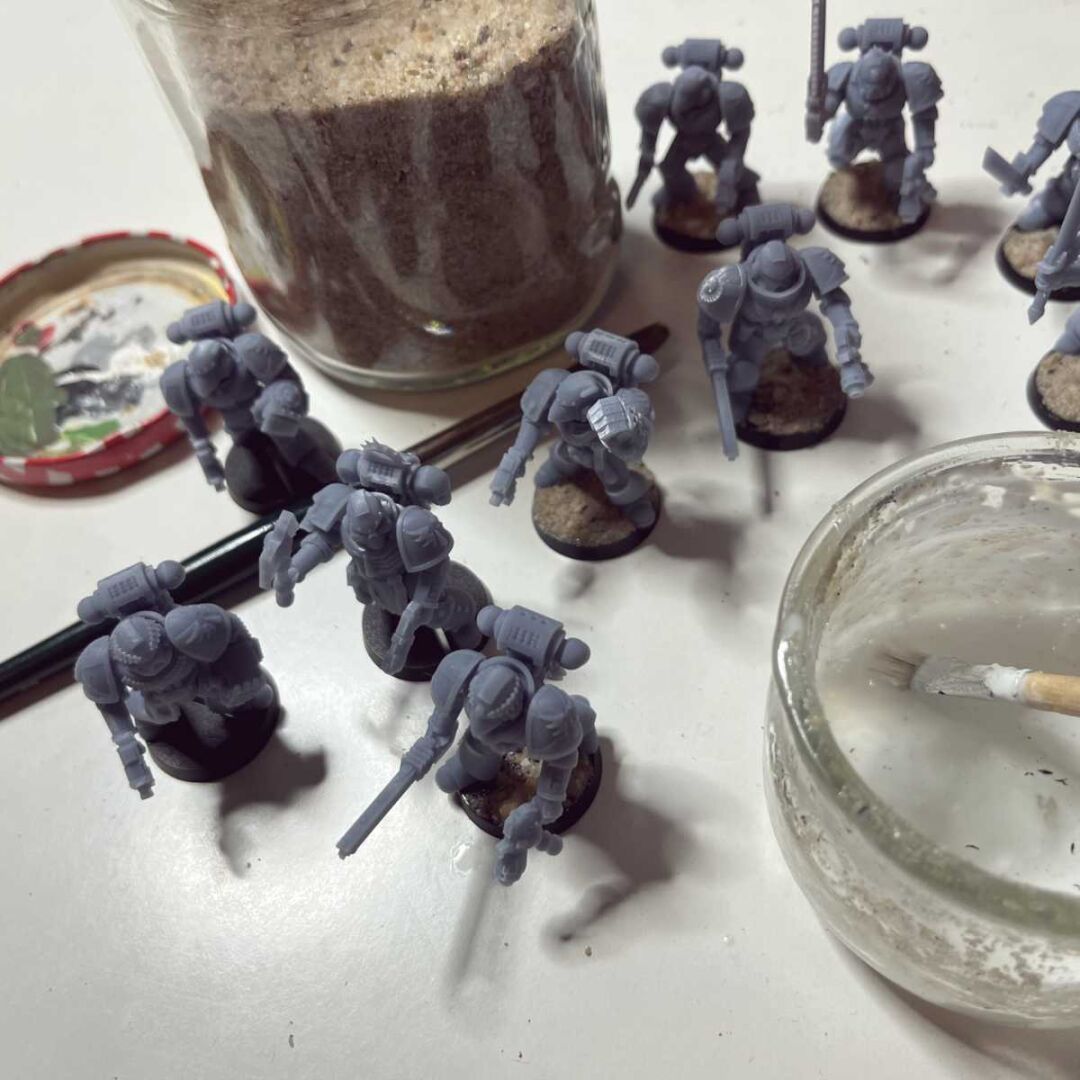 Picture of miniatures for the Warhammer 40000 game, some having sand glued to their bases, some have not.