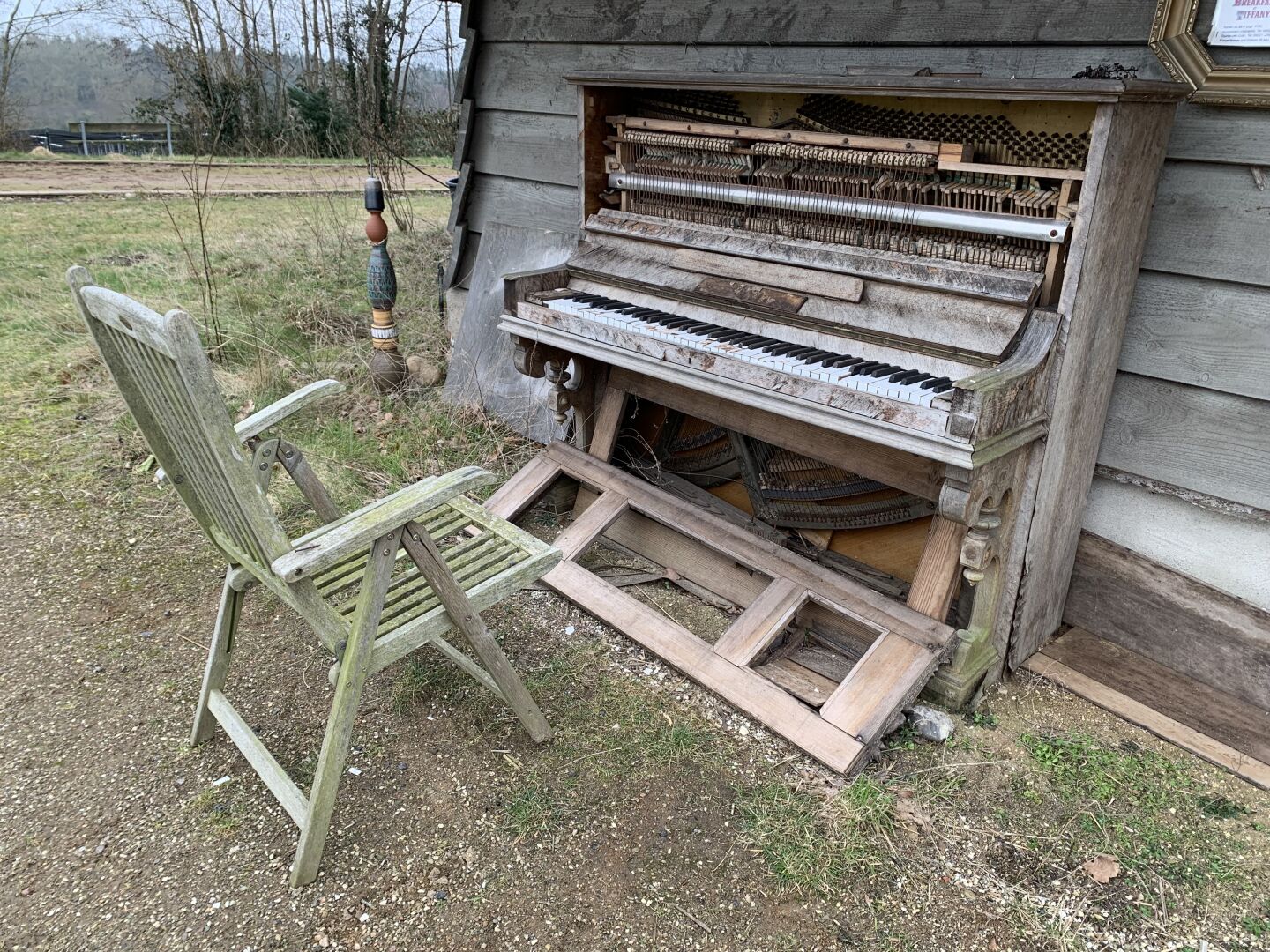 Ein altes Klavier, draußen vor einer Bretterwand, verwittert, offensichtlich monatelang dem Wetter ausgesetzt gewesen.