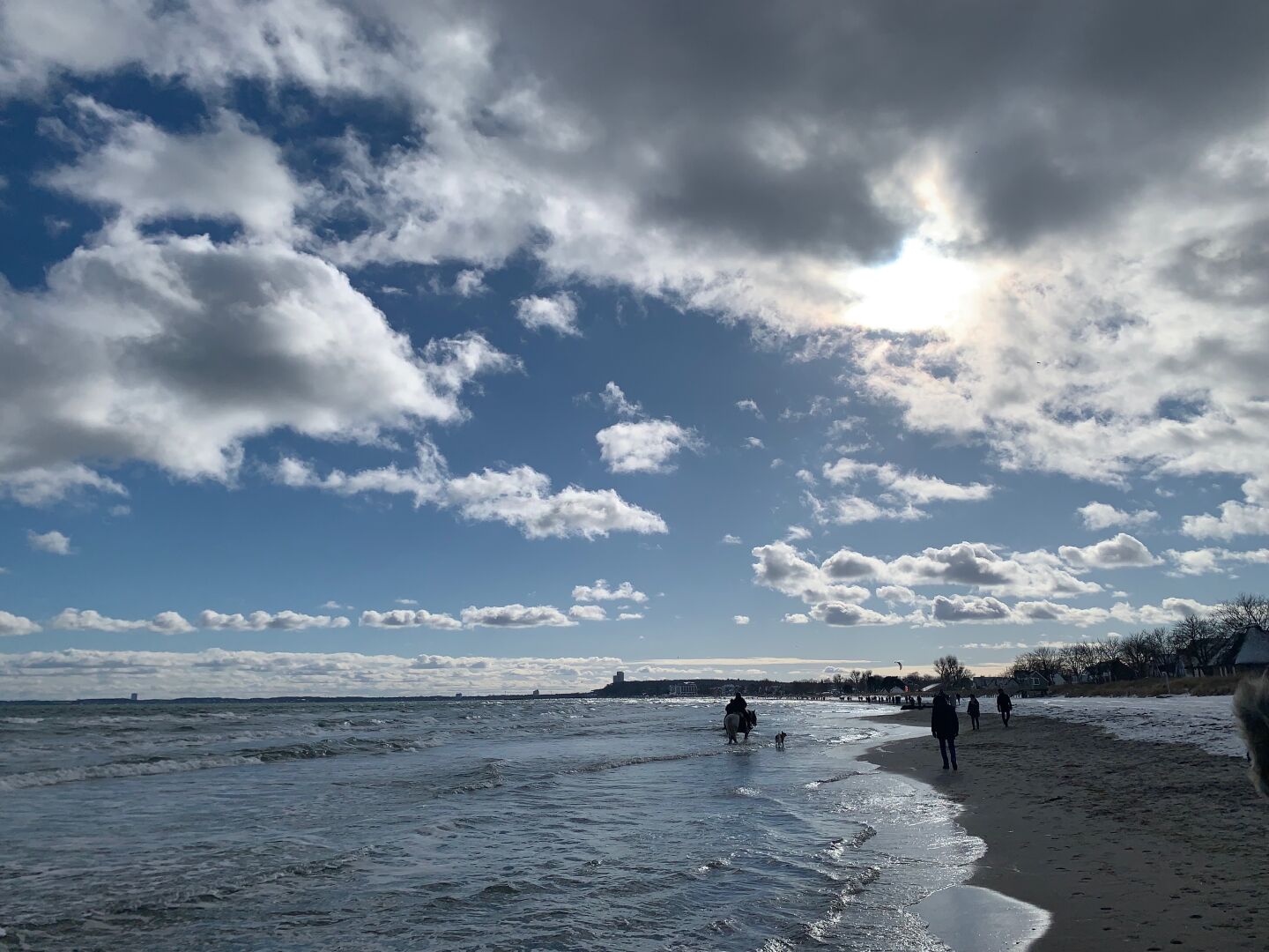 Blick auf den Strand zwischen Haffkrug und Scharbeutz: es ist sonnig, große Wolken sorgen für dramatisches Aussehen. Viele Spazierengehende unterwegs.