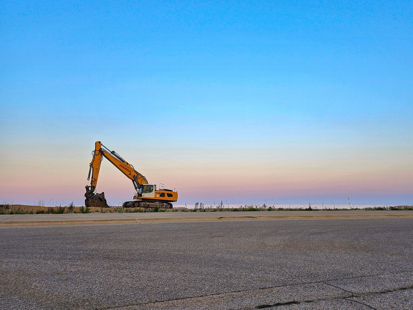 An excavator on the beach at sunset