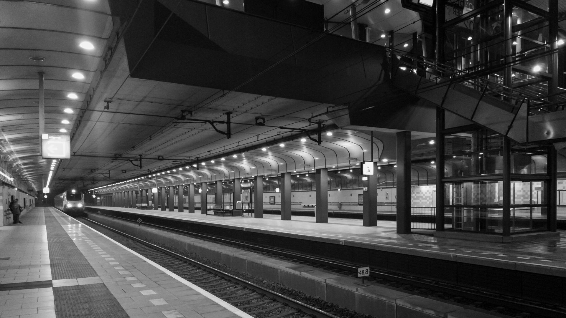 Perron van een ondergronds treinstation met doorkijk naar trap en bovenste verdieping.