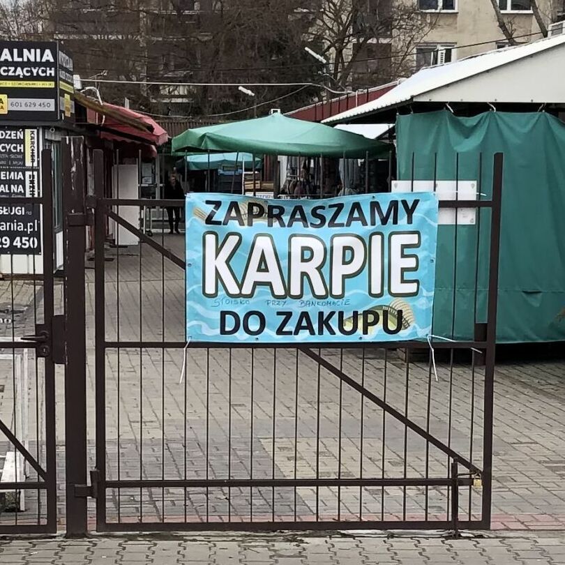 Baner na bramie bazarku z hasłem: „Zapraszamy karpie do zakupu” / Banner on the gate of the market with the slogan: "We invite carps to shop"