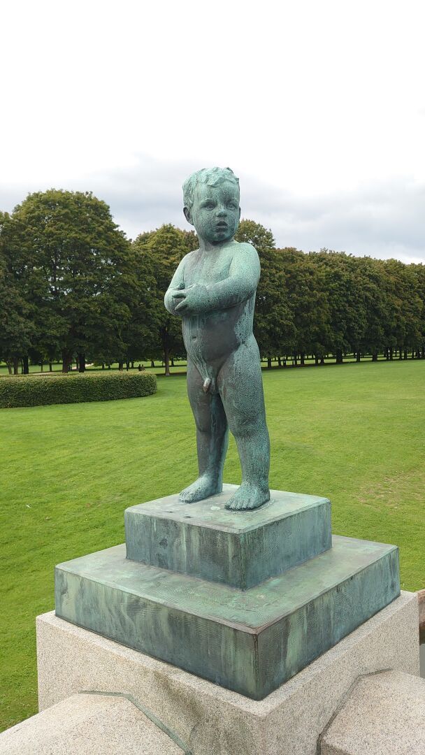 A statue of a naked child. One hand is clasping the other in front of his chest, and he look to his left, as if he's a bit worried or expecting.