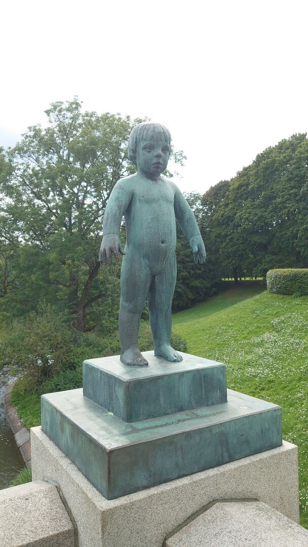 Staute of a naked child. She's standing holding her arms straight down at her sides, a bit away from her body. The face is expressionless.