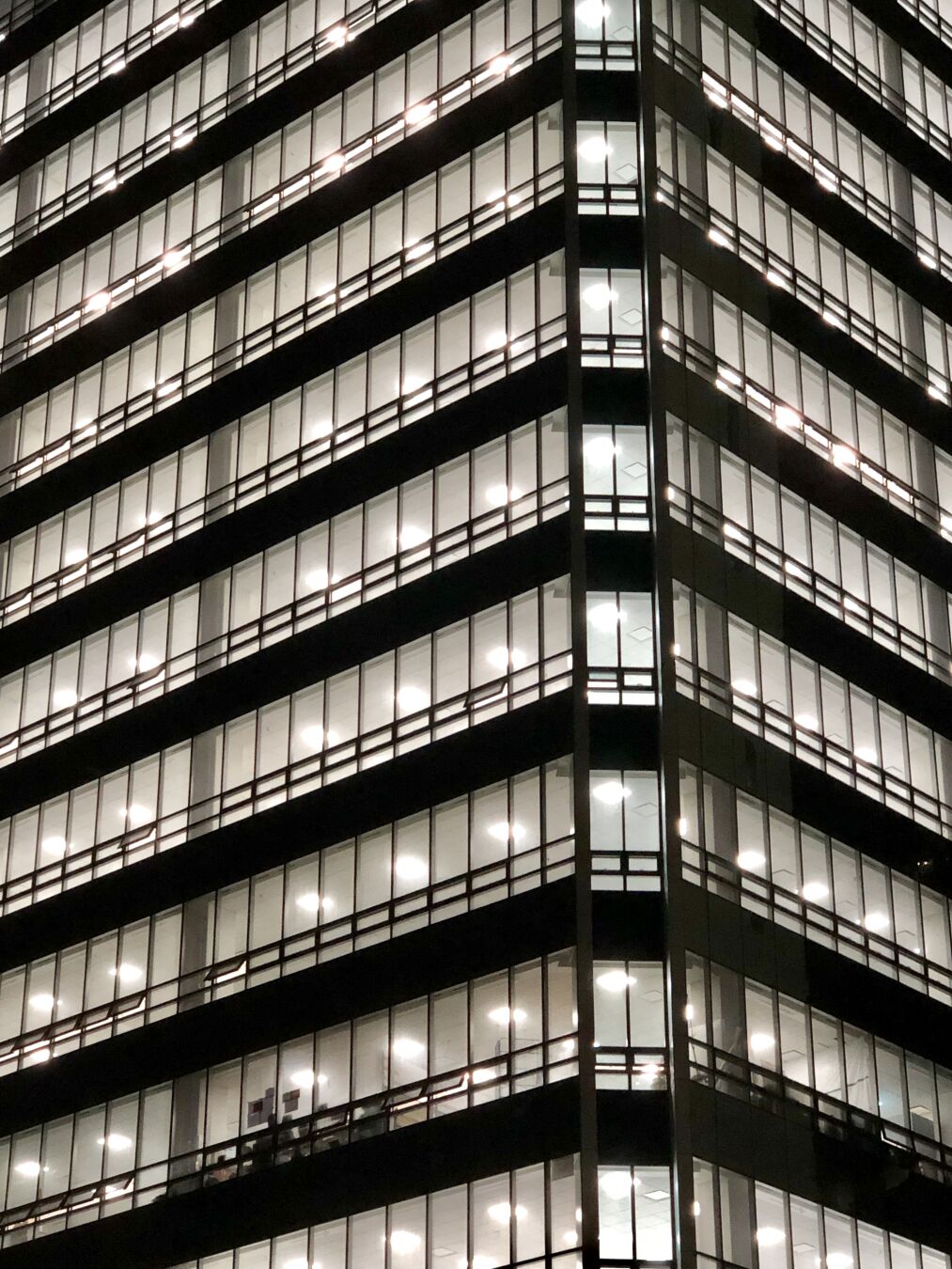 Ein Hochhaus bei Nacht. Alle Fenster sind beleuchtet während die Fassade dunkel ist, wodurch der Eindruck eines Schwarz-Weiß-Bilds entsteht.