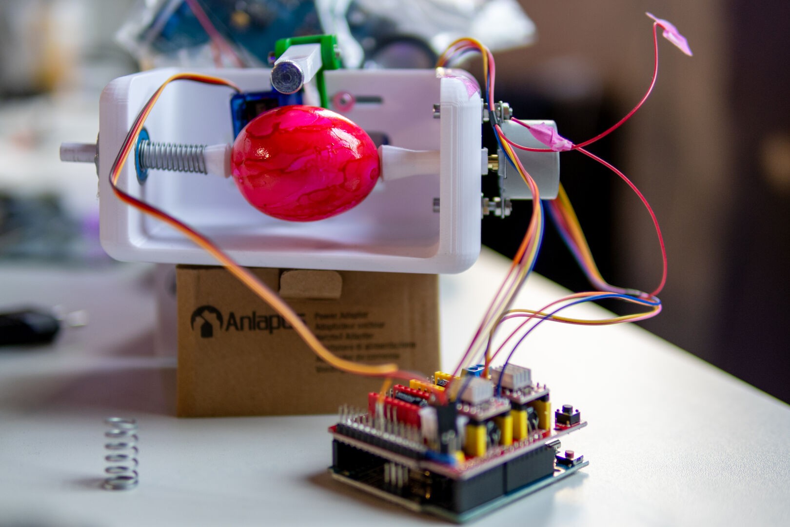 Ein Eggbot. Eine 3D-gedruckte Vorrichtung, mit der Eier bemalt werden können. Die Steuerelektronik ist im Vordergrund zu sehen.