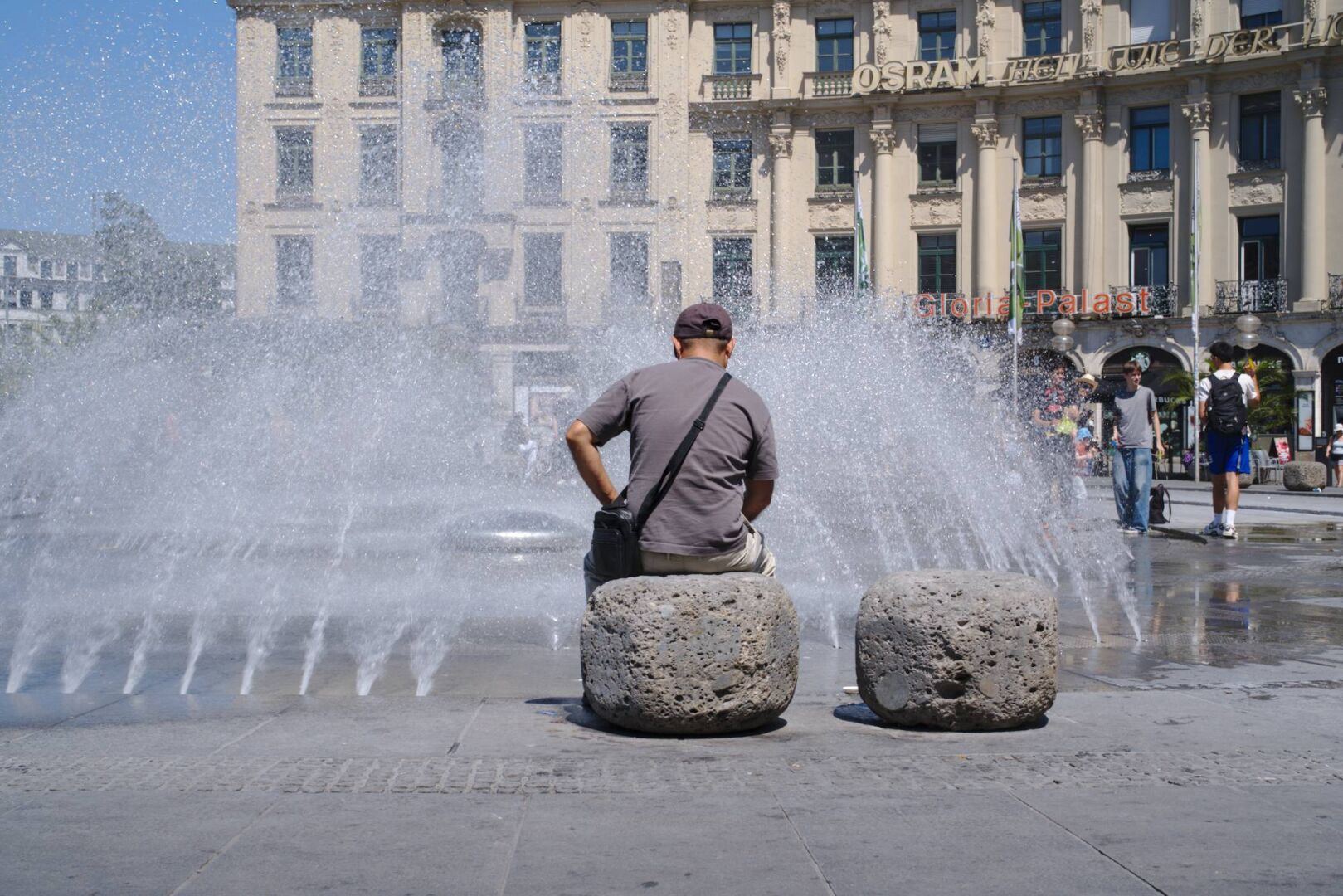 persons looking at a fountain on a hot day in the city