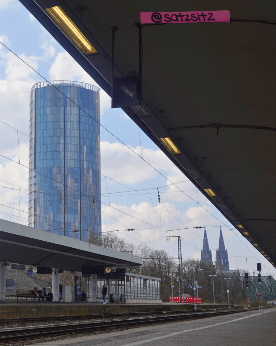 Am Seufzer Bahnhof. Der Dom guckt in der Ferne zwischen Gleis unten und Gleisdach oben durch