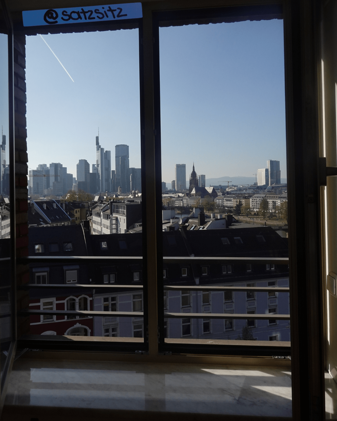 Geöffnetes Fenster, durch das die Skyline von Frankfurt bei blauem himmel zu sehen ist.