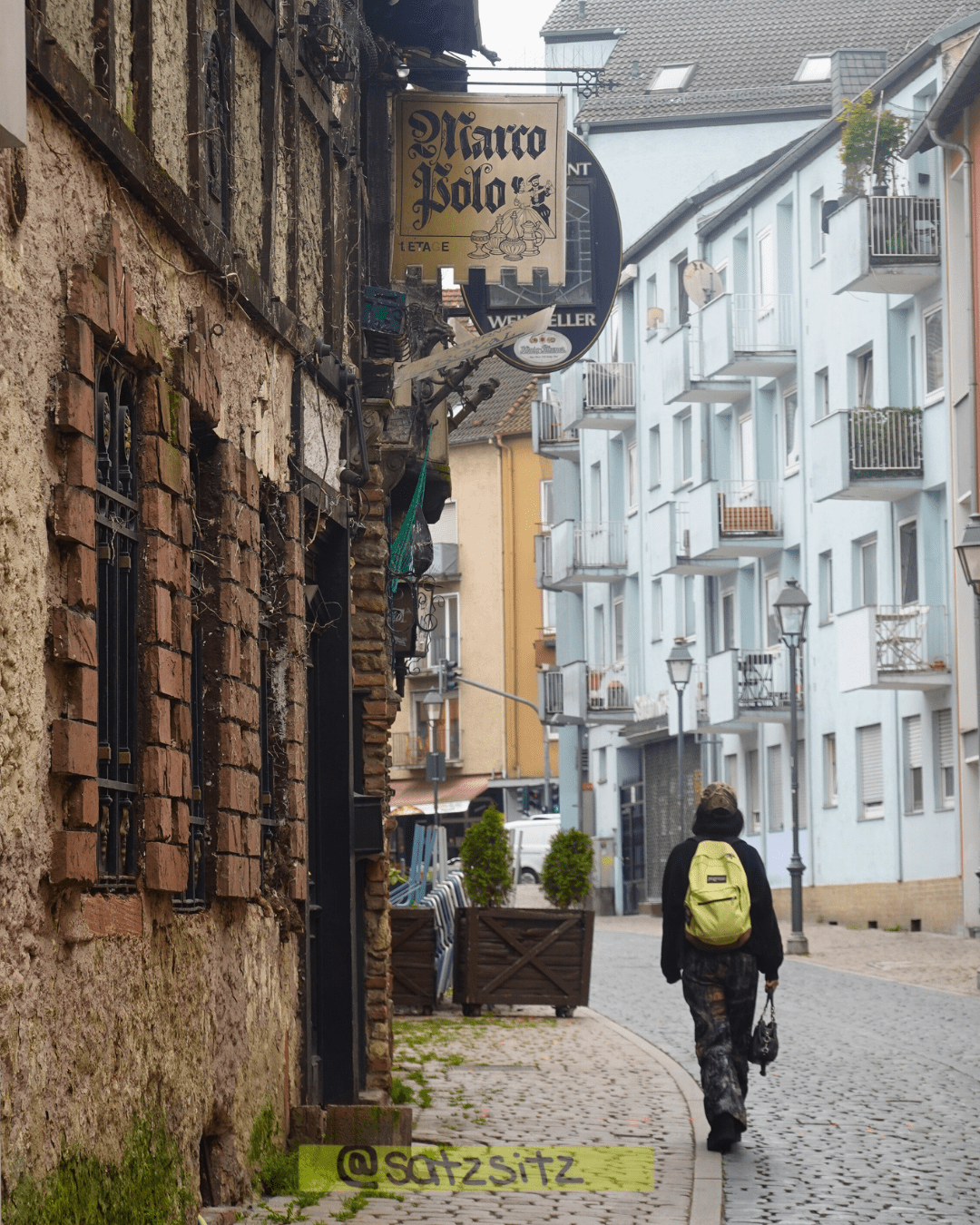 Eine Person läuft über Kopfsteinpflaster in Sachsenhausen an einem alten gebäude vorbei, das Marco Polo heißt.