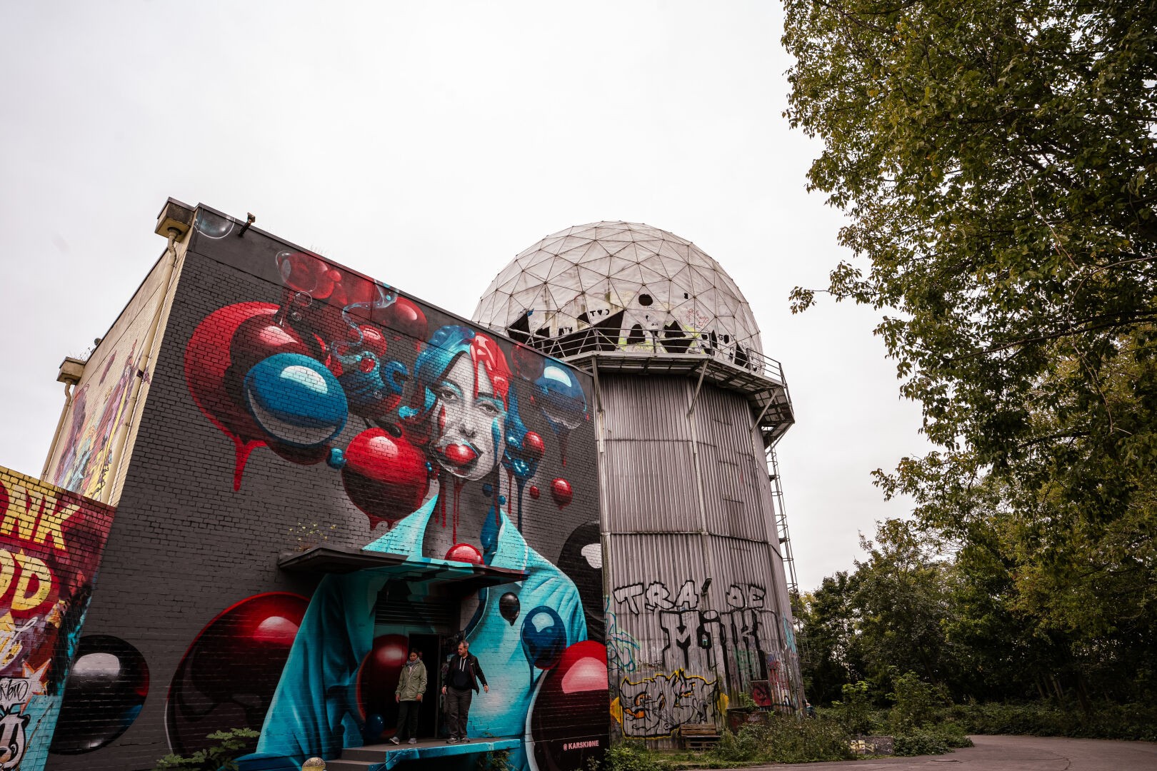 The cupola building from the outside, with another building in the front. The building in the front has a spectacular graphiti painting of a woman and bubbles on it.
