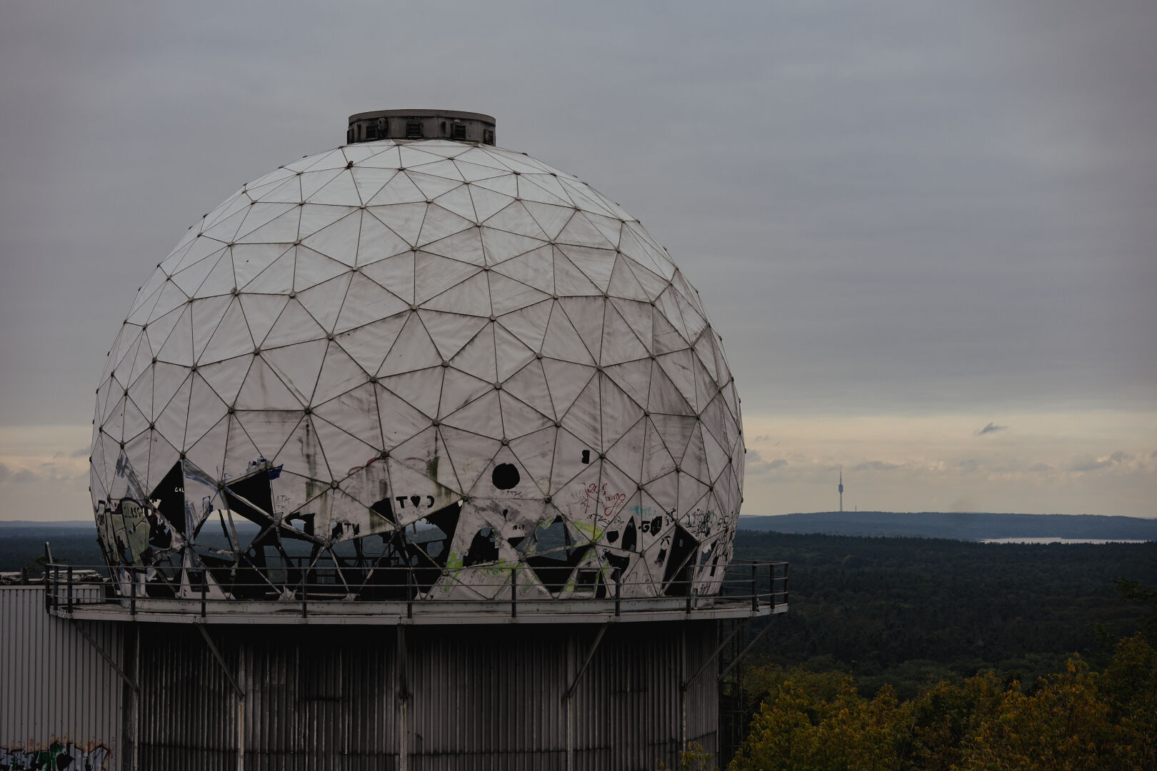 Landscape shot of the cupola building of the Teufelsberg and a wide landscape in the back. On the horizon, there is a TV tower. Sky is cloudy.