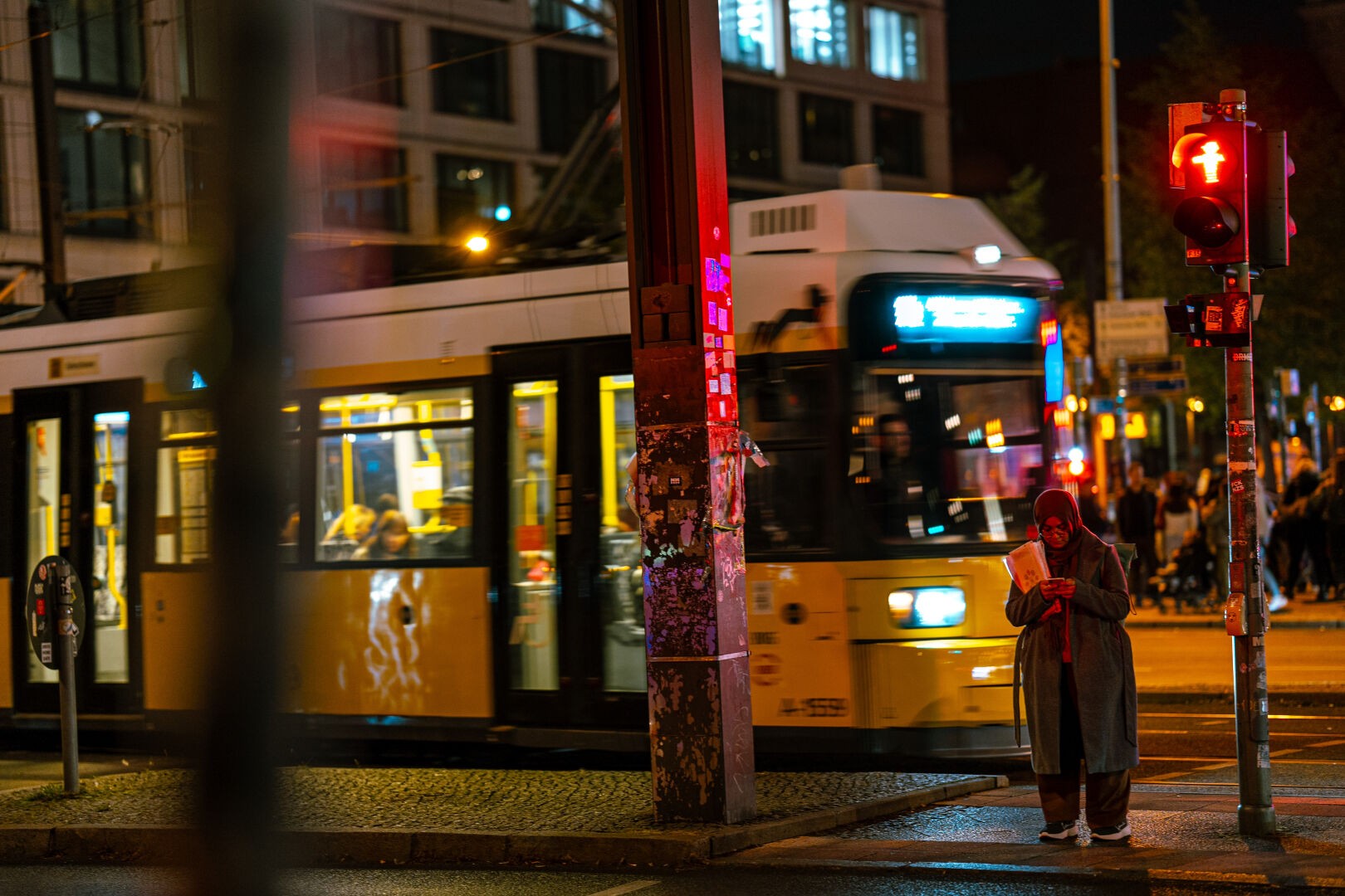 Nightscape of a passing Tram in movement. A person is waiting for a red light to turn green.