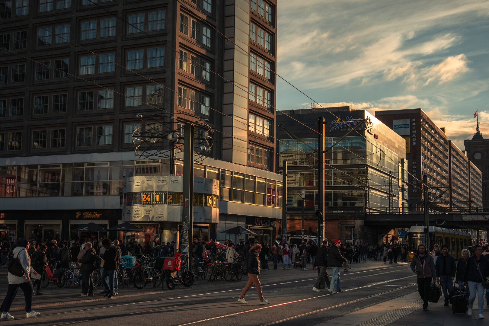 Image of the Alexanderplatz with the world clock (Weltuhr) during golden hour. Many people walking around and a tram in the background.