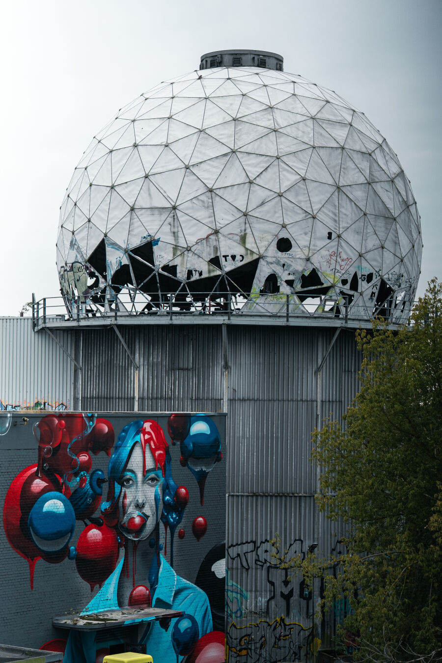 Another closeup shot of one of the buildings, with a very distinct graffiti in the front facing wall of the building. The image shows a red & blue haired woman chewing gum and making red and blue bubbles.
