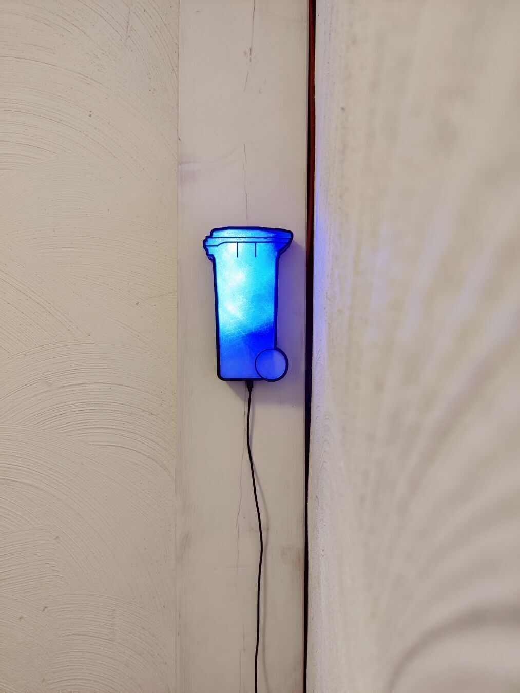 A translucent miniature, wall-mounted trashcan. It glows blue