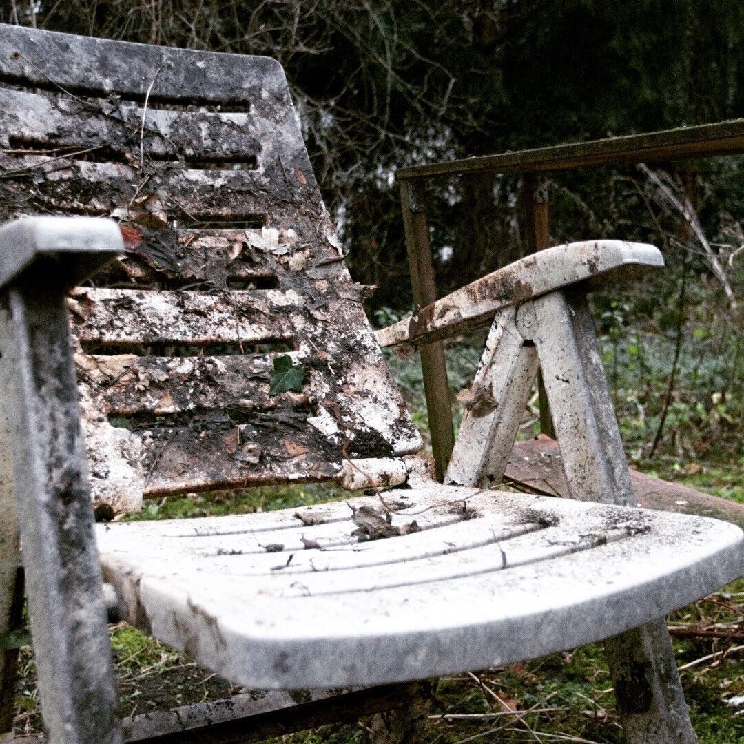 Ein Plastikstuhl, der verrottet und von der Natur mit Laub besetzt ist.