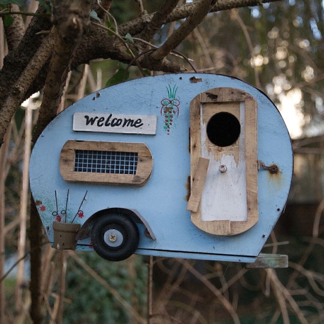 Ein Vogelhaus im Stil eines Wohnwagens. Einige Holzteile fallen bereits ab.