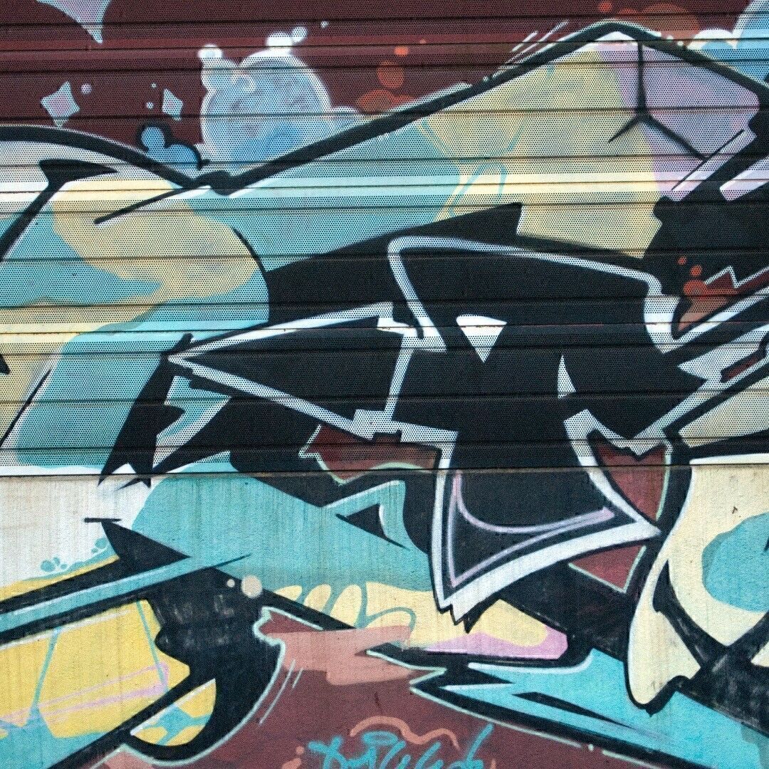 Ein sehr farbenfrohes graffiti auf einem gelochten Schallschutzblech eines Bahndamms.