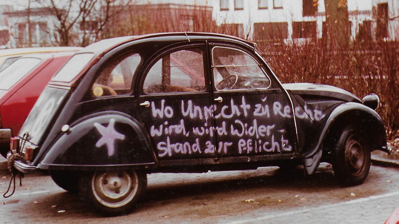 dunkelblauer 2 CV (Ente) mit lilafarbener Aufschrift: wo Unrecht zu Recht wird, wird Widerstand zur Pflicht.