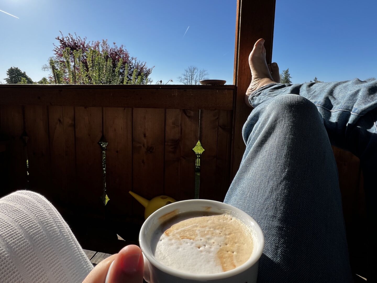 sitting barefoot on a sofa on my balcony, holding a cappuccino and looking at the blue sky and the sun.